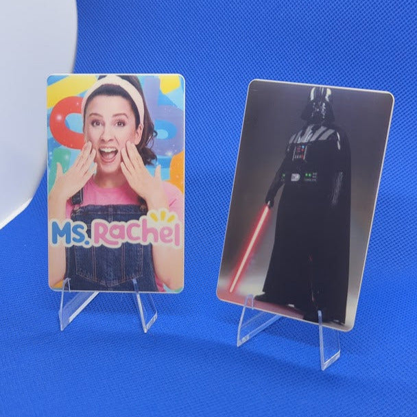 Two cards on stands, one with a colorful design and text, the other with a black and white character, against a blue background.